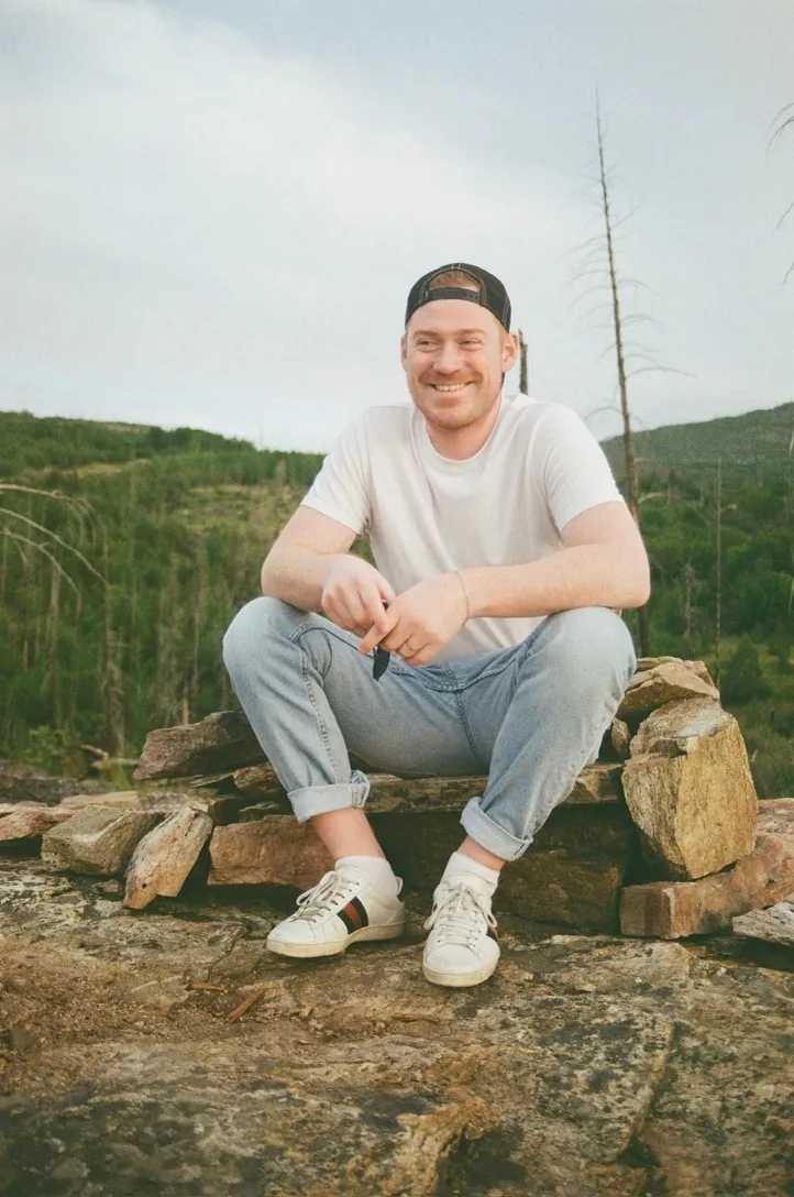 Spencer Claydon, founder of Sidetrack, sitting outdoors on a rocky hillside.